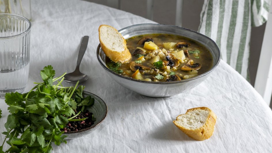 Тарелка супа из белых грибов стоит на столе рядом с кусочками хлеба и зеленью