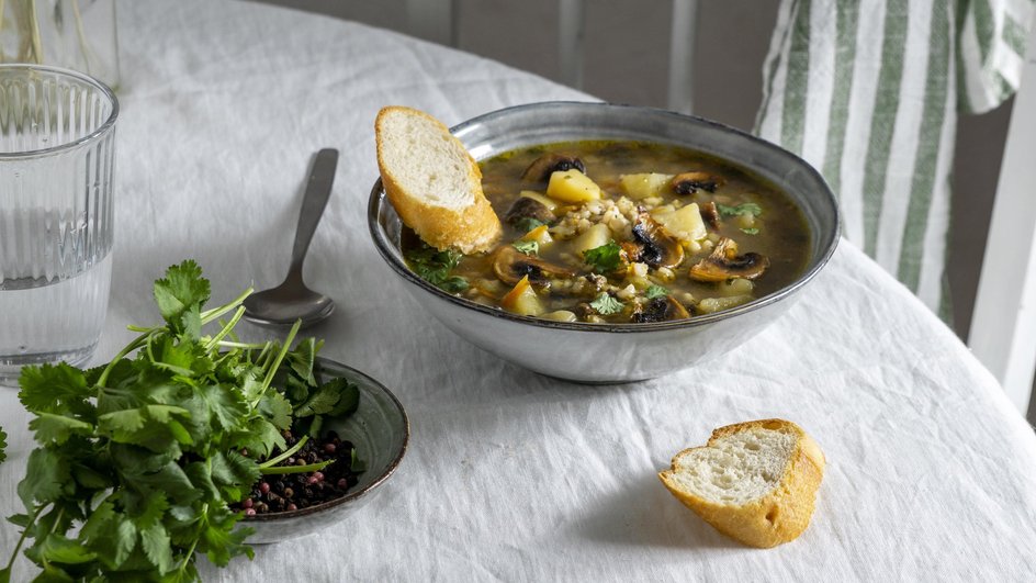 Тарелка супа из замороженных сморчков стоит на столе рядом с кусочками хлеба и зеленью Тарелка супа из замороженных сморчков стоит на столе рядом с кусочками хлеба и зеленью