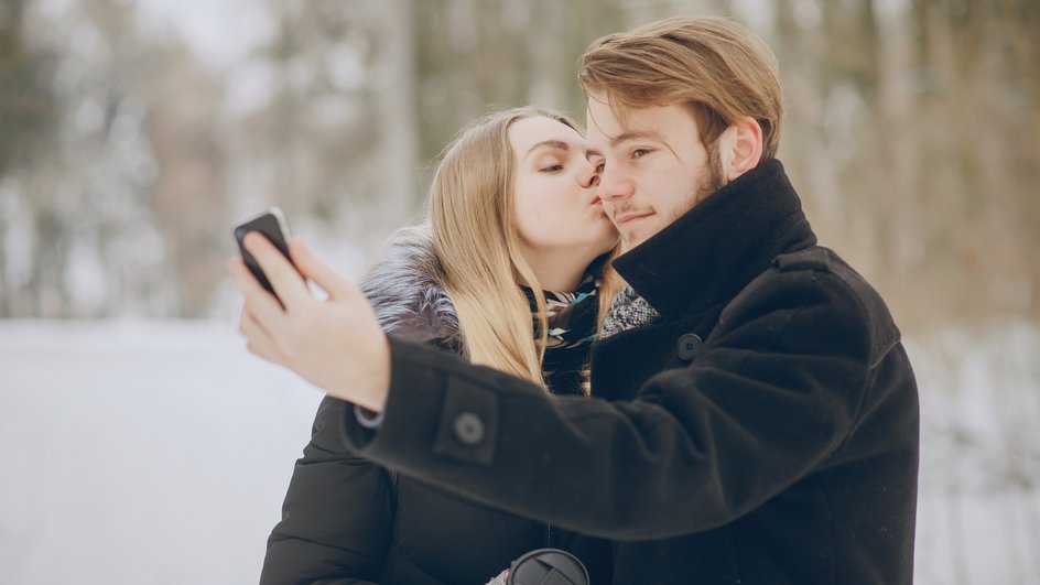 Мужчина делает селфи, когда девушка целует его в благоприятный день по любовному гороскопу