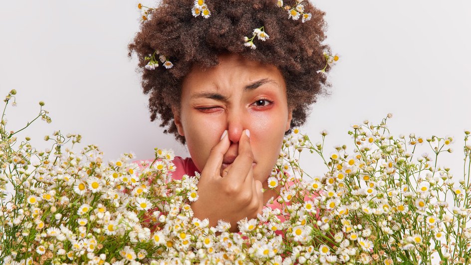 Девушка с красными глазами зажимает нос в окружении цветов 
