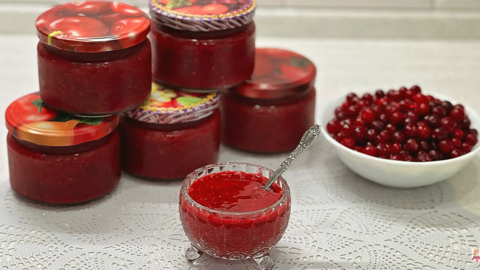 Банки и креманка варенья из клюквы с лимоном стоят рядом с тарелкой клюквы Банки и креманка варенья из клюквы с лимоном стоят рядом с тарелкой клюквы