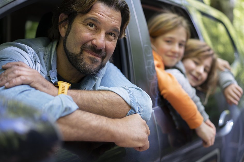 Отец и двое детей выглядывают из окон большого автомобиля