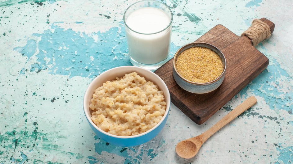Тарелка пшеничной каши стоит на столе рядом со стаканом молока и пшеничной крупой Тарелка пшеничной каши стоит на столе рядом со стаканом молока и пшеничной крупой