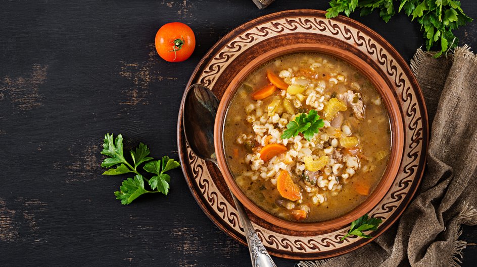 Тарелка постной солянки с солеными огурцами и перловкой стоит на столе Тарелка постной солянки с солеными огурцами и перловкой стоит на столе