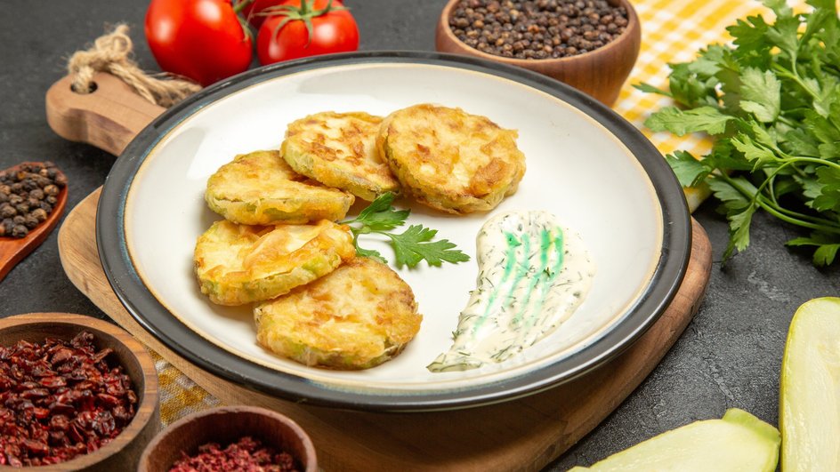 Драники с кабачком, приготовленные в духовке, лежат на тарелке рядом с соусом и ингредиентами