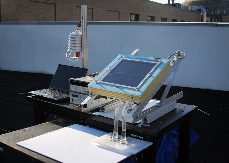 Прототип новой двухступенчатой ​​системы сбора воды (в центре справа) испытали на крыше MIT. Устройство, которое было подключено к ноутбуку для сбора данных и было установлено под углом к ​​солнцу, имело черную пластину для сбора солнечной энергии, а производимая им вода стекала в две трубки внизу. Фото: Алина ЛаПотин