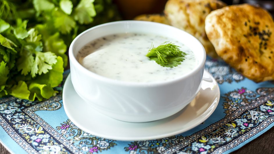 Тарелка окрошки с копченой курицей на сметане стоит на столе рядом с зеленью Тарелка окрошки с копченой курицей на сметане стоит на столе рядом с зеленью
