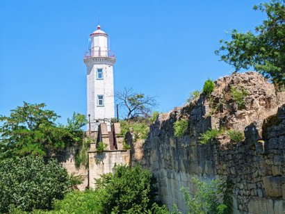 Белый маяк среди каменистых стен и деревьев