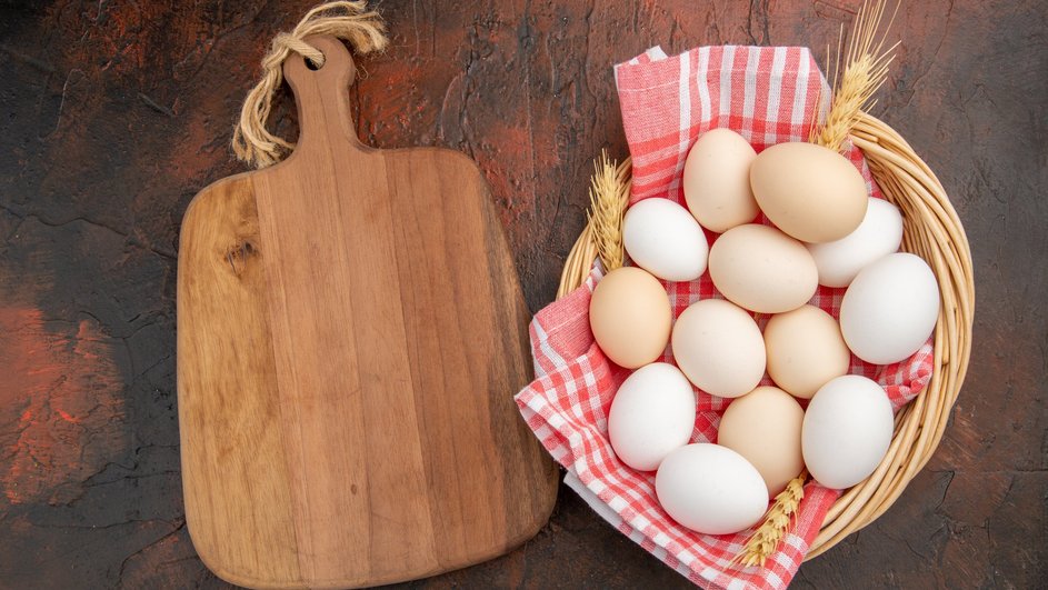 Яйца лежат в плетёной корзинке рядом с доской 