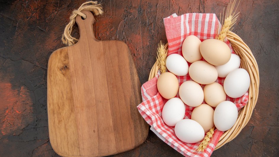 Яйца лежат в плетеной корзине рядом с кухонной доской