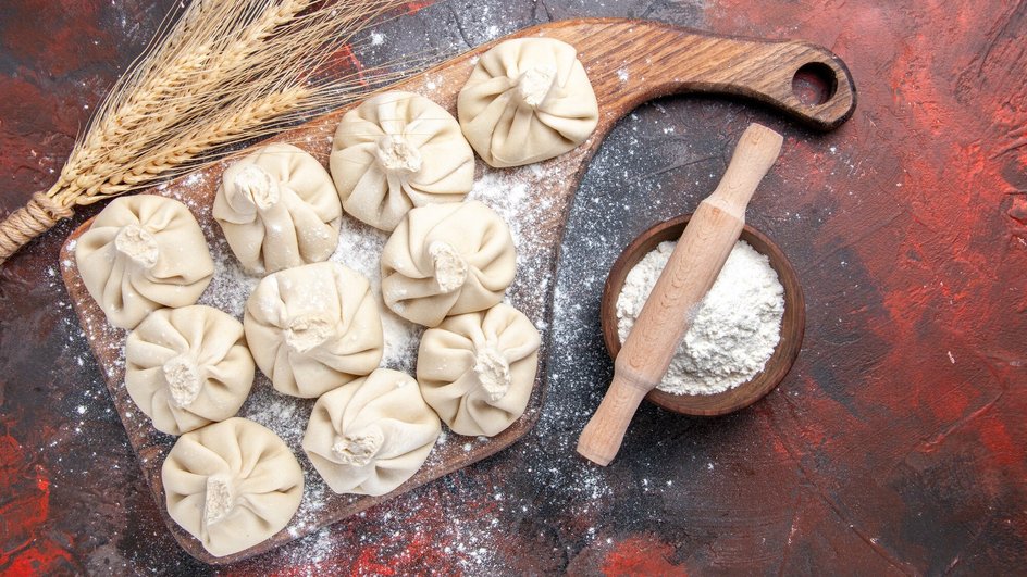 Сырые хинкали с картофелем лежат на доске рядом с мукой