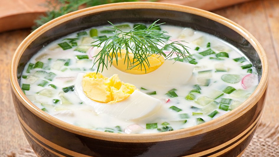 Тарелка окрошки на майонезе с колбасой, украшенной яйцом и зеленью, крупным планом Тарелка окрошки на майонезе с колбасой, украшенной яйцом и зеленью, крупным планом