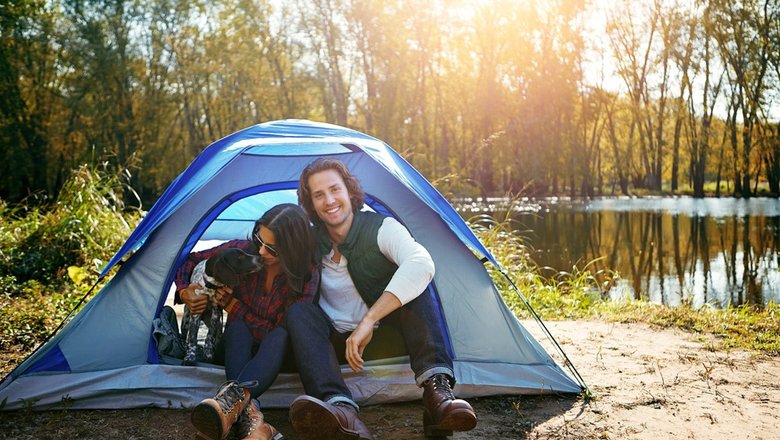 Мужчина и женщина ночуют в синей палатке с собакой в отпуске.