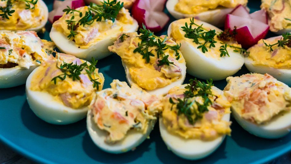 Фаршированные яйца с грибами и морковкой, украшенные зеленью, лежат на тарелке