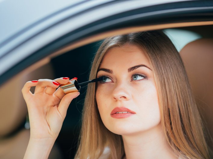 Девушка красит ресницы тушью в автомобиле