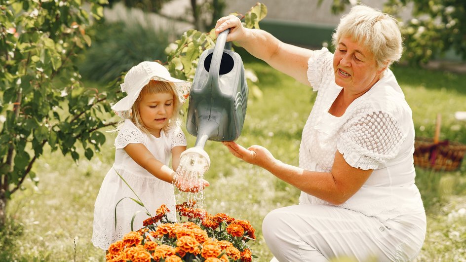 Бабушка и девочка в белой одежде поливают цветы