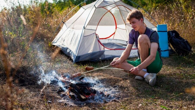 Мужчина готовит на привале рядом с палаткой во время велопутешествия.