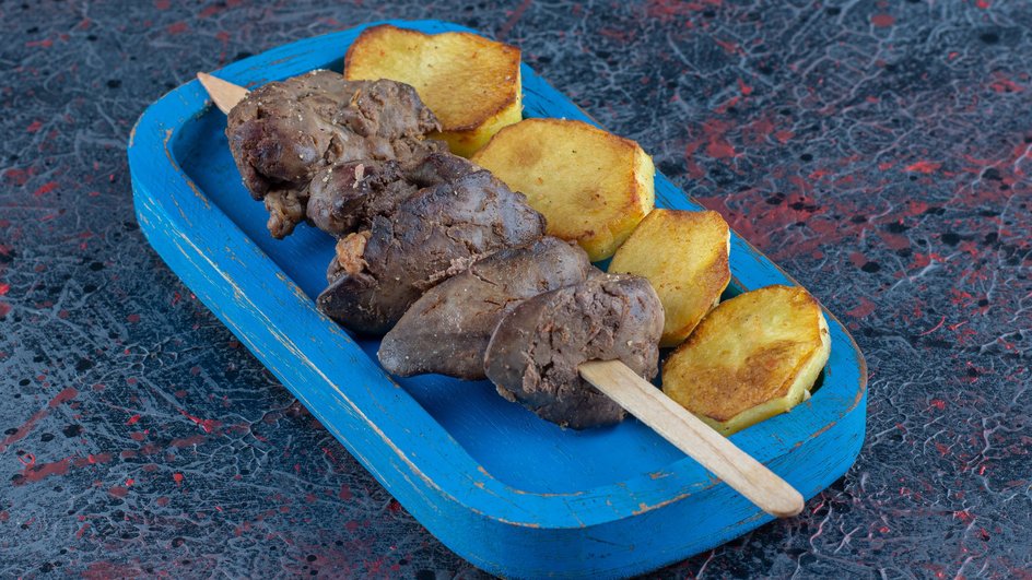 Жареная печень на шпажке с ломтиками картофеля на синей деревянной тарелке Жареная печень на шпажке с ломтиками картофеля на синей деревянной тарелке