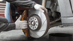 Рабочий осматривает тормозную систему автомобиля в автосервисе