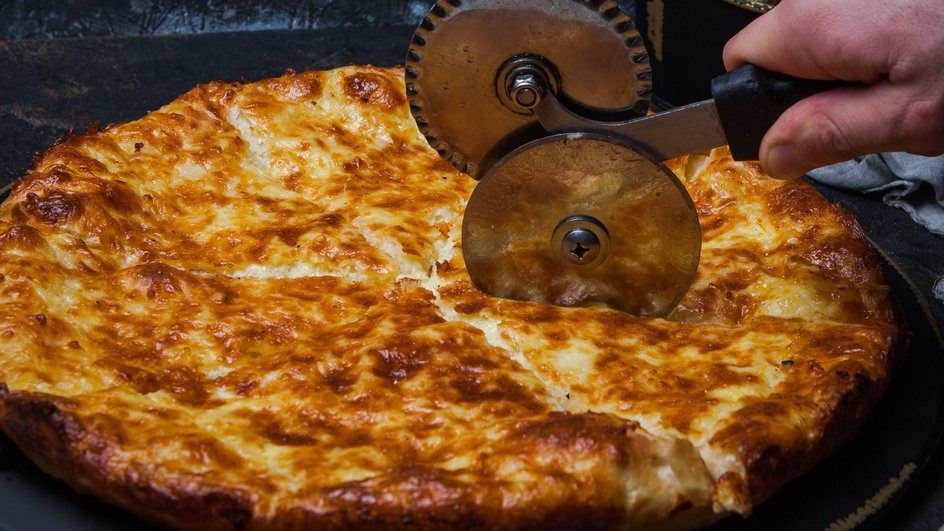 Мужчина разрезает лепешку с сыром, картофелем и зеленью Мужчина разрезает лепешку с сыром, картофелем и зеленью