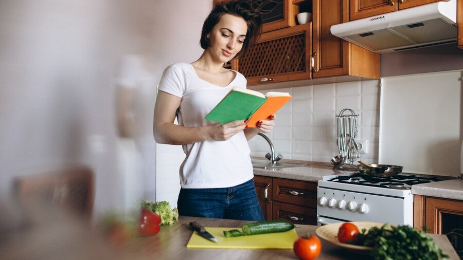 Девушка с поваренной книгой на кухне Девушка с поваренной книгой на кухне
