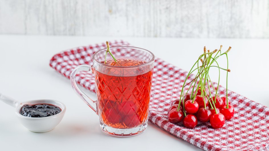 Компот из вишни и смородины в стакане с рядом лежащими ягодами 