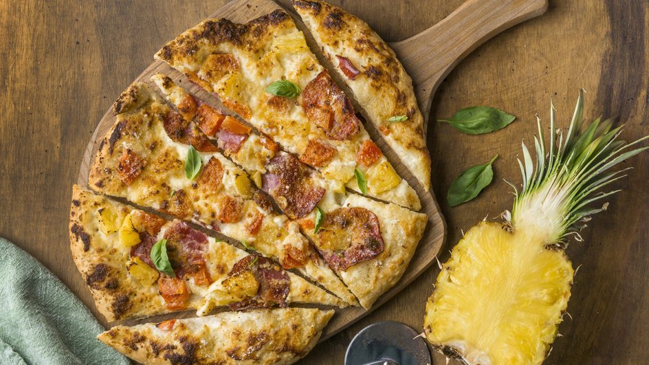 Нарезанная пицца с ананасами лежит на доске рядом с ананасом