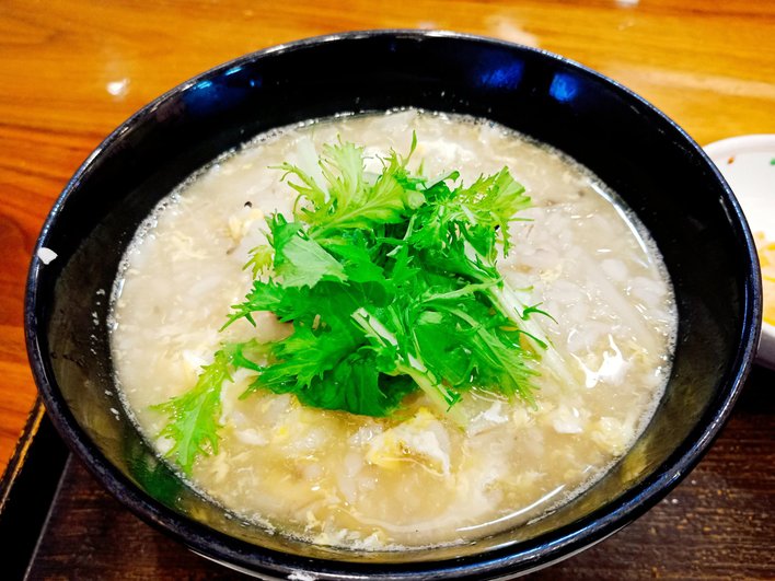 Кислые щи с курицей, украшенные зеленью, в глубокой черной тарелке стоят на деревянном столе Кислые щи с курицей, украшенные зеленью, в глубокой черной тарелке стоят на деревянном столе