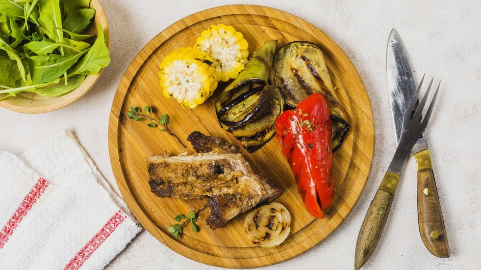 Стейк из говядины с овощами, приготовленный на гриле, лежит на подставке рядом со столовыми приборами