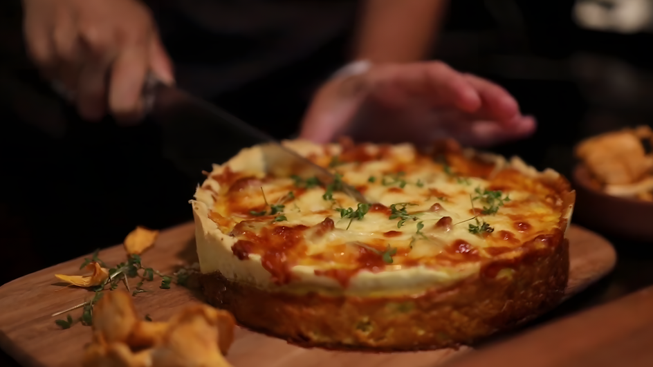 Человек ножом разрезает постный киш с лисичками и картофелем на деревянной доске Человек ножом разрезает постный киш с лисичками и картофелем на деревянной доске