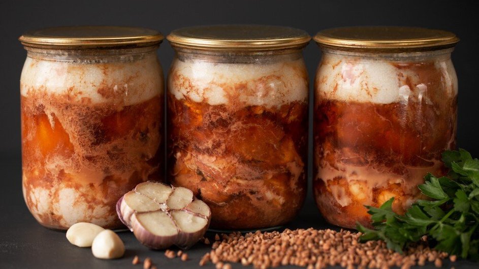 Три банки с тушеным мясом, рядом - чеснок, перец горошком рассыпан и зелень Три банки с тушеным мясом, рядом - чеснок, перец горошком рассыпан и зелень