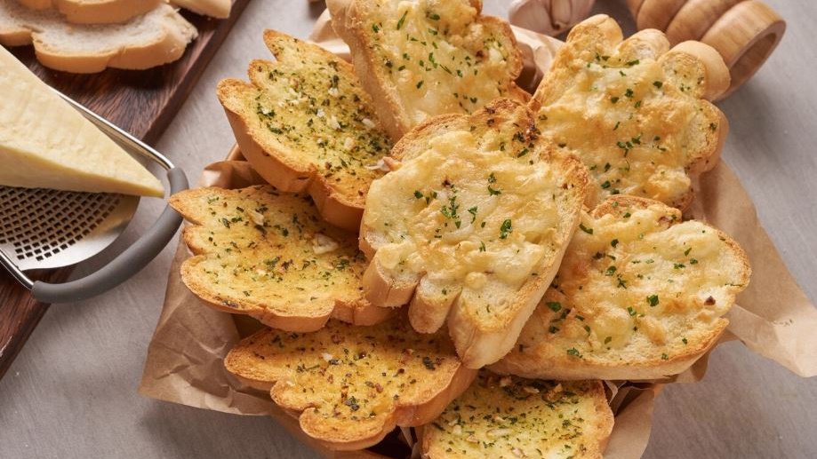 Запеченные в духовке гренки с чесноком и сыром на кухонном столе Запеченные в духовке гренки с чесноком и сыром на кухонном столе