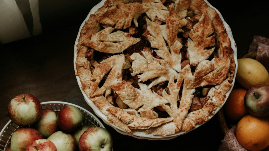 Шарлотка лежит в блюде на столе рядом с яблоками