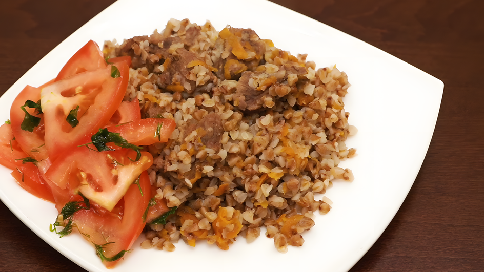Тарелка гречки с мясом и помидорами крупным планом Тарелка гречки с мясом и помидорами крупным планом