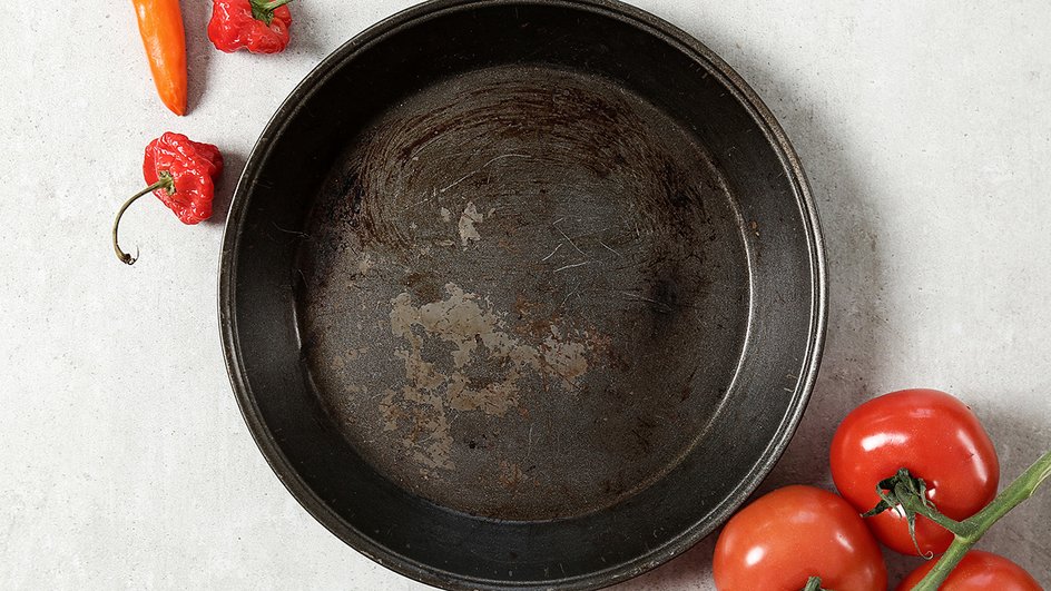 Сковорода с испорченным покрытием стоит на столе рядом с перцем и помидорами 