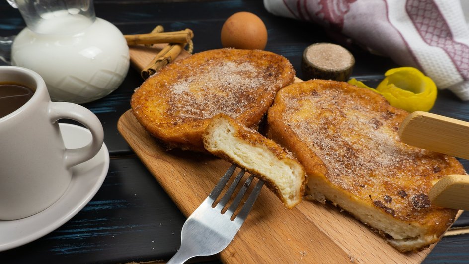 Сладкие гренки лежат на доске рядом с чашкой чая и половинкой гренки на вилке
