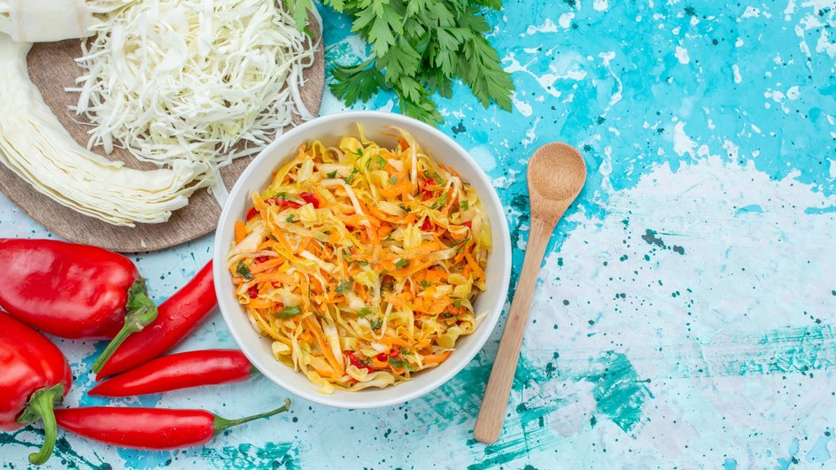 Салат с корейской морковью, капустой и болгарским перцем лежит на тарелке рядом с ингредиентами