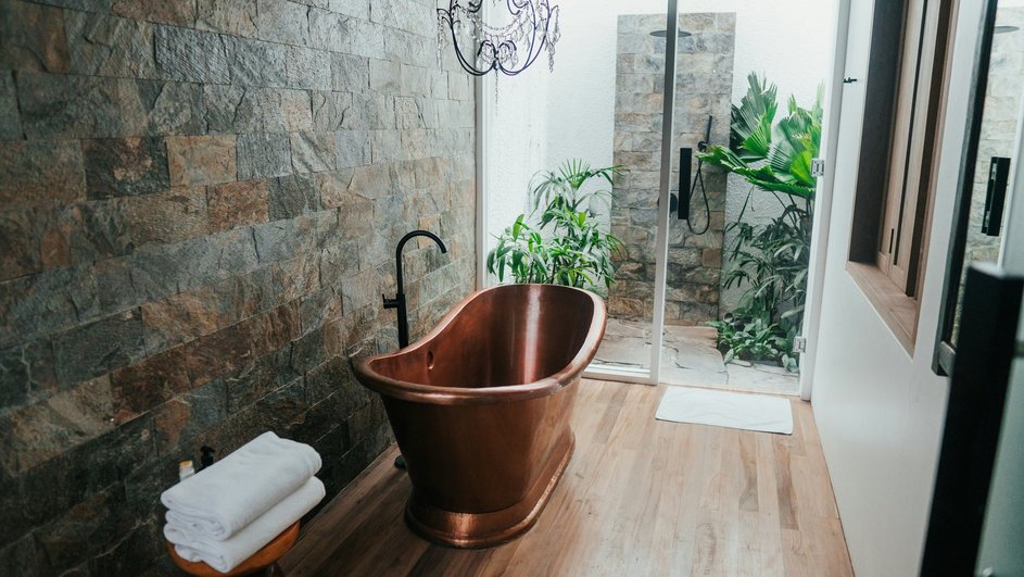 Бронзовая ванная с полотенцами и коричневой стеной на фоне стеклянной двери