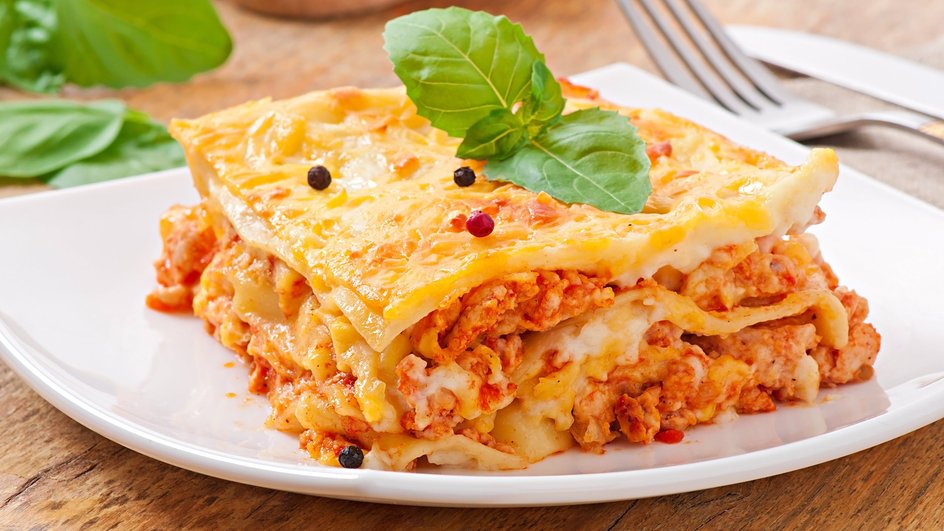 Кусочек лазаньи с фаршем и соусом болоньезе лежит на тарелке Кусочек лазаньи с фаршем и соусом болоньезе лежит на тарелке