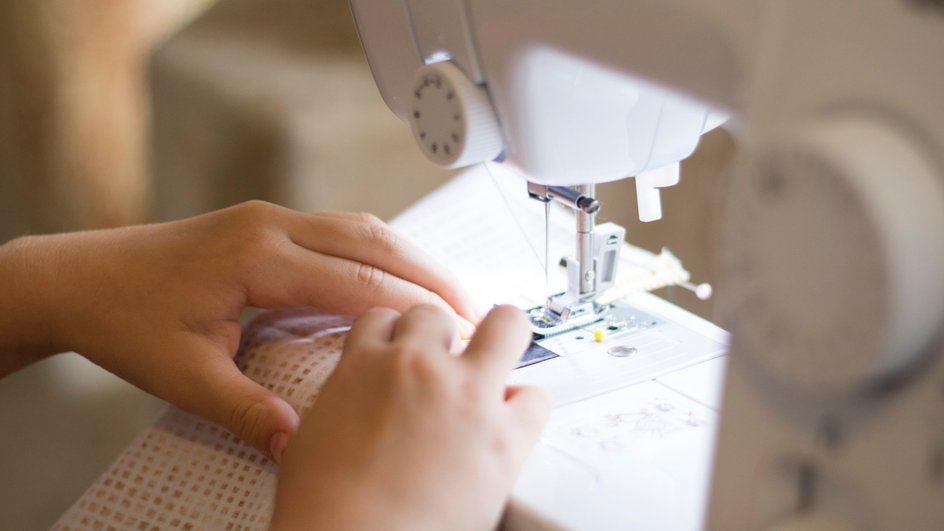 Руки прошивают ткань на швейной машинке 