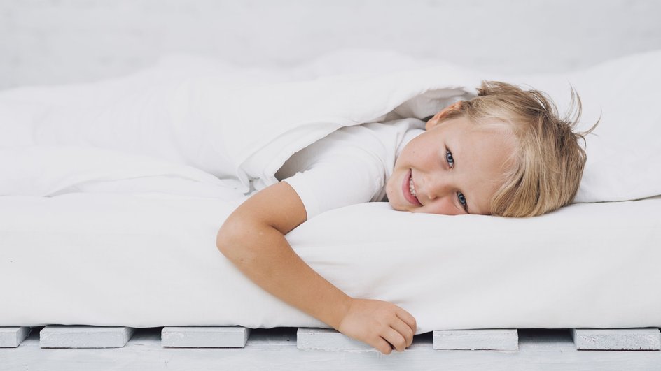 Ребенок лежит в белой постели на матрасе и улыбается