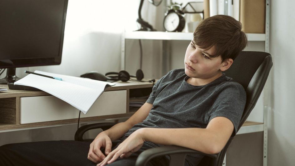 Подросток грустит позируя на фоне рабочего стола