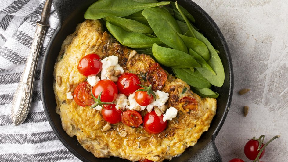Вкусный овсяноблин без молока лежит на сковороде с овощами Вкусный овсяноблин без молока лежит на сковороде с овощами