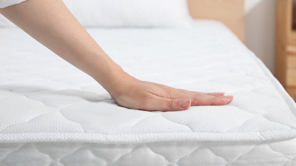 Рука трогает белый матрас на фоне кровати
