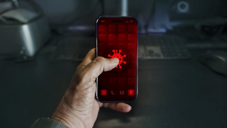 Мужчина держит в руках телефон на Android, на котором горит красная иконка вируса