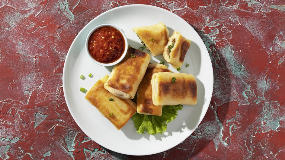Блины грибами и мясным фаршем лежат на тарелке рядом с соусом Блины грибами и мясным фаршем лежат на тарелке рядом с соусом