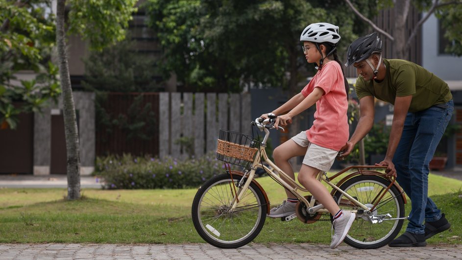 Отец помогает дочери учиться езде на велосипеде