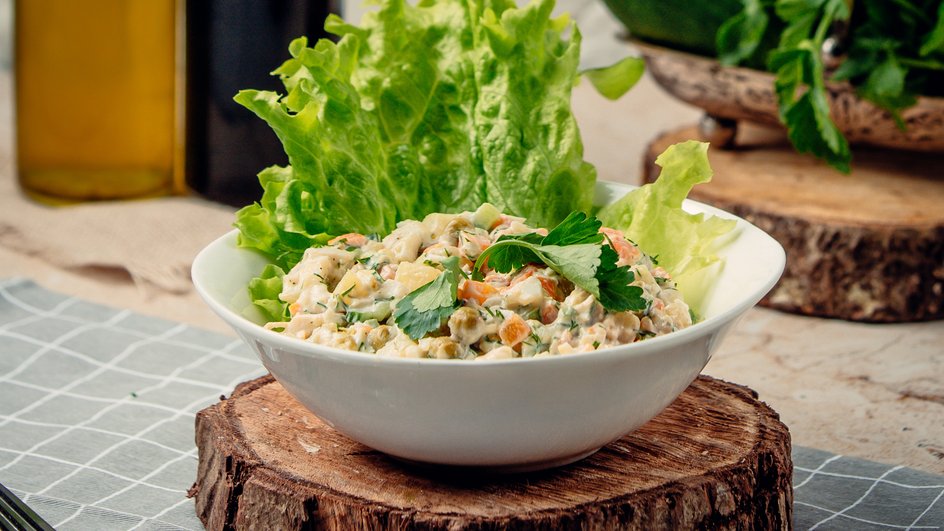 Салат с шампиньонами и яйцами, украшенный зеленью, в тарелке на деревянной подставке Салат с шампиньонами и яйцами, украшенный зеленью, в тарелке на деревянной подставке