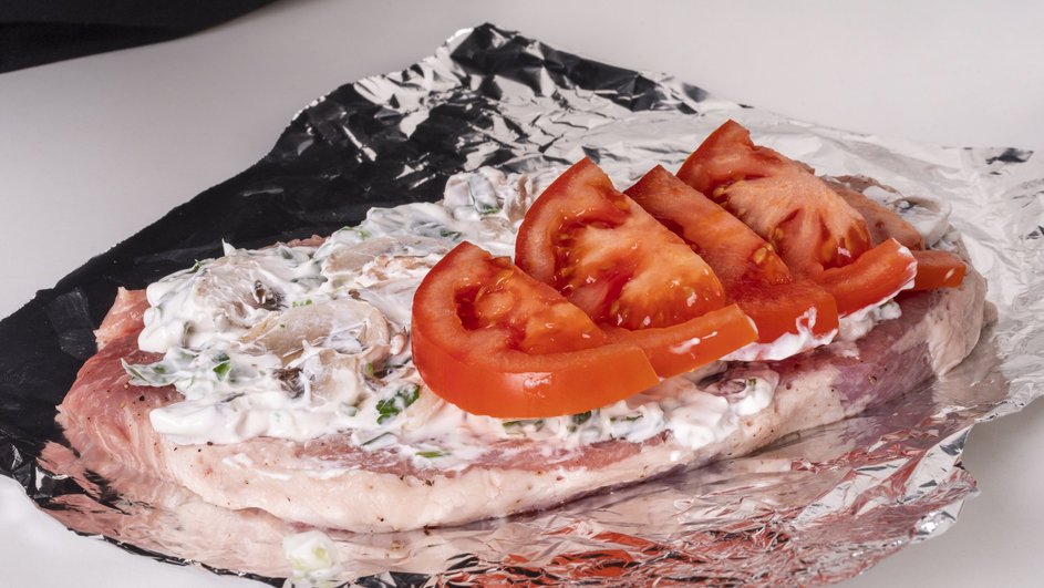 Сырое мясо с соусом и помидорами лежит на фольге Сырое мясо с соусом и помидорами лежит на фольге
