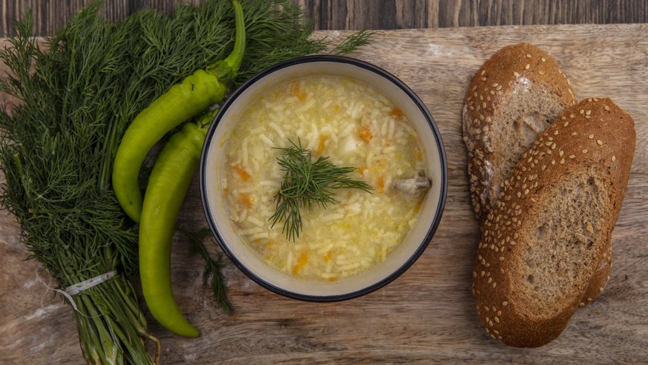 Классические щи, украшенные зеленью, стоят на деревянной доске рядом с зелеными перцами, пучком укропа и парой кусочков хлеба Классические щи, украшенные зеленью, стоят на деревянной доске рядом с зелеными перцами, пучком укропа и парой кусочков хлеба